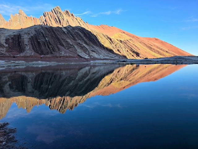 Jagged red rocky mountains reflecting in the still morning waters of Laguna Hampococha, Peru.