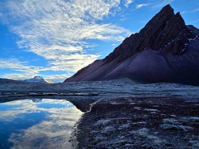 The triangular, jagged Chachacomayoc Peak reflecting in the icy morning waters of Huampococha Lake near Ausangate, Peru.