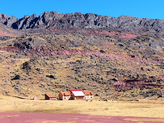 Huampococha Lodge dwarfed by towering, red rocky mountains rising behind it.