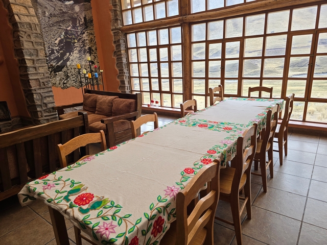 Inside view of Chillca Lodge, showing a large table with hand-emboridered tablecloth, and huge picture windows looking out toward Ausangate Mountain.