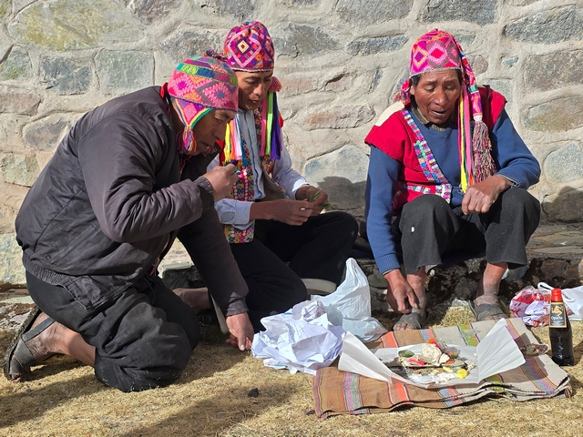 Three Andean men receive prepare offerings of coca leaves, sweets, wool, and more during a Pachamama ceremony at the base of Peru's Apu Ausangate.
