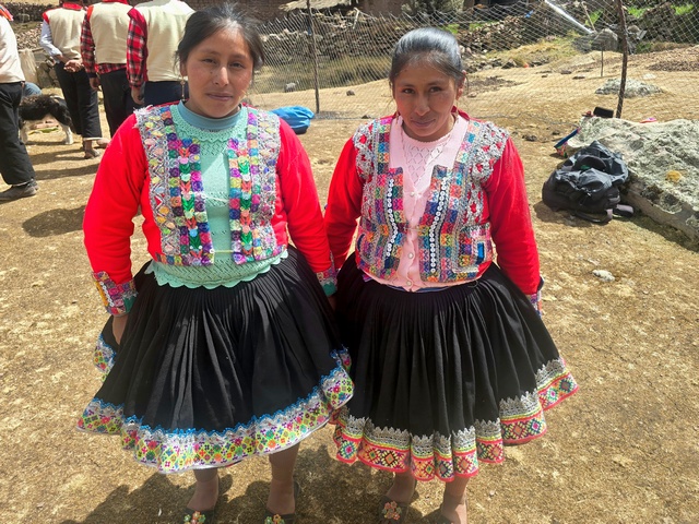 Two Andean women in traditional dress, with black skirts and bright red, hand-woven tops.